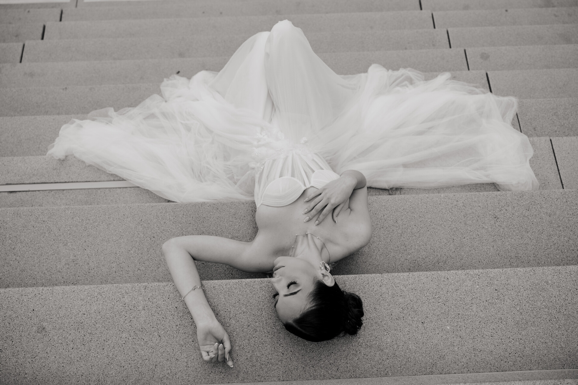 Stilvolle Braut in hochwertigem Designer-Brautkleid liegt auf einer Steintreppe – Symbol für Exklusivität, Handarbeit und den emotionalen Wert eines hochwertigen Brautkleids ab 1.500 € bei Brautfreundin.